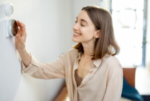 Woman happily adjusts thermostat for winter energy efficiency. Follow winter energy saving tips from Family Heating & Cooling in Westport, MA for a cozy and cost-effective home. Insulate, seal gaps, optimize thermostat, perform maintenance, harness solar heat, upgrade appliances, and embrace zone heating.