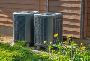 Air conditioning units outside a residential home with yellow flowers growing nearby, representing the importance of regular AC maintenance and timely repairs to prevent sudden breakdowns. Family Heating and Cooling provides expert AC troubleshooting and repair services in New Bedford, Fall River, and surrounding areas. Contact us now for help with AC not cooling, why did my air conditioner stop working, air conditioning repair near me, air conditioner troubleshooting, AC unit failure, HVAC repair services, AC malfunction fix, broken AC repair, emergency air conditioner service, air conditioning not turning on, why is my AC blowing hot air, air conditioner compressor repair, fixing a non-working air conditioner, air conditioning repair in \[location], HVAC technician near me, affordable AC repair, residential AC services, air conditioning unit inspection, cooling system issues, air conditioning problems, air conditioner maintenance, AC repair services near me, cooling unit issues, AC maintenance, expert HVAC repair, home air conditioning solutions, Family Heating and Cooling services in New Bedford, Fall River, Taunton, Dartmouth, Somerset, Fairhaven.
