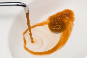 Running faucet showing rusty or discolored hot water with brown and orange tint caused by water heater corrosion, sediment buildup, or aging plumbing pipes, indicating potential need for water heater repair, plumbing inspection, and water quality troubleshooting by Family Heating, Cooling, Electric and Plumbing. Contact us today for help with rusty or discolored hot water, brown hot water from tap, orange water from faucet, yellow water coming from sink, dirty hot water problem, hot water discoloration issues, why is my hot water brown, rusty water from water heater, water heater rust contamination, sediment in hot water tank, corroded water heater symptoms, anode rod failure water heater, water heater repair near me, plumbing inspection near me, water quality issues home plumbing, emergency plumber near me discolored water, hot water heater flushing service, water heater maintenance near me, residential plumbing services near me, water heater replacement near me, hot water smells metallic or rusty, inconsistent water color faucet, galvanized pipe rust water issues, whole house water discoloration troubleshooting, Family Heating Cooling Electric and Plumbing water heater service, licensed plumber water discoloration repair near me, emergency water heater diagnostics, hot water not clear repair service, home plumbing corrosion inspection near me.