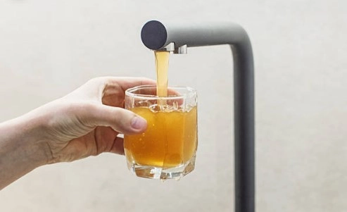 Hand holding a glass under a tap pouring brown, polluted water.
