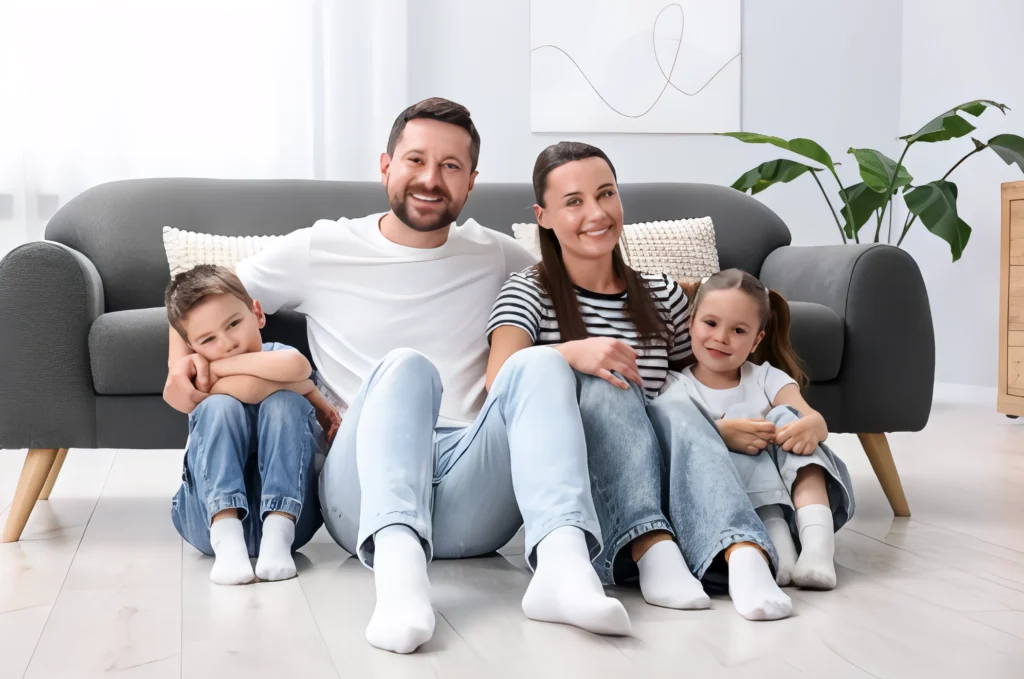 Happy family sitting on the floor by a central heat pump in a cozy living room.