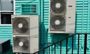 Three mini split outdoor units mounted on a turquoise wall.