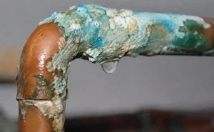 Corroded copper pipe with green patina and water droplet